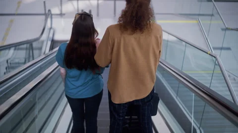 Two Travelers Going Down Escalator with Shared Bag at Airport Stock Footage 334566206