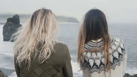 Two traveling women standing on the black beach, bear troll toes rocks in Stock Footage