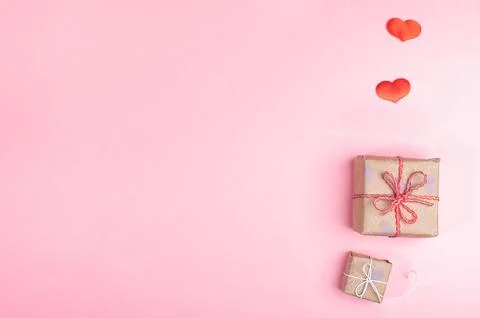 Two trendy diy wrapped gift boxes and two red hearts on pink background. Va.. Stock Photos