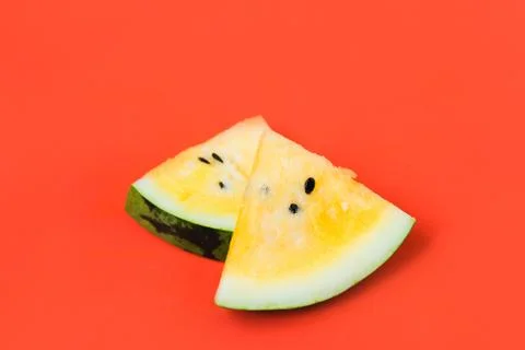 Two triangular slices of ripe yellow watermelon on a red background Stock Photos