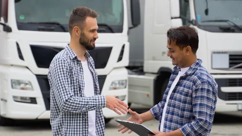 Two truck drivers shaking hands on truck parking. Hispanic manager and Indian Stock Footage 251843232