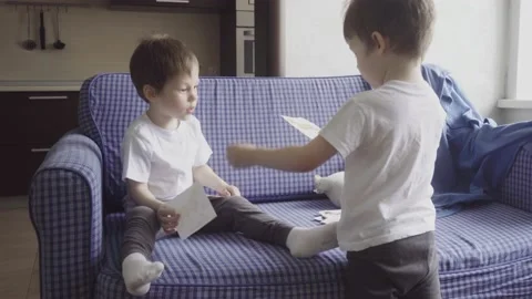 Two twin boys spend time together at home, sit on couch and play Stock Footage 189875500