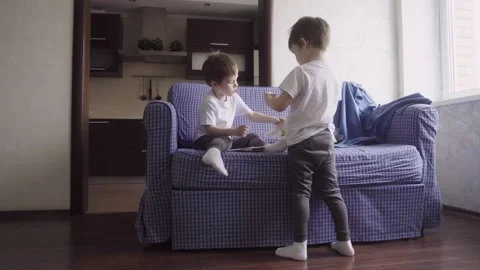 Two twin boys spend time together at home, sit on couch and play Stock Footage 189875782