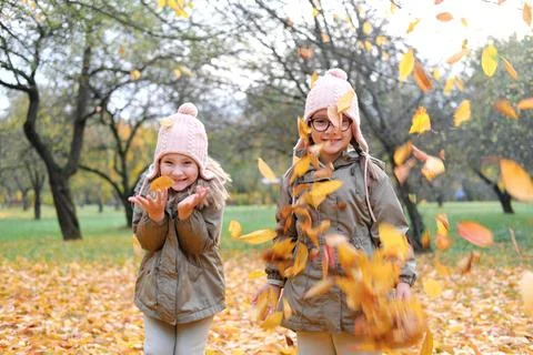 Two twin girls throw up a large armful of autumn leaves. Girls have fun in .. Stockfoto's