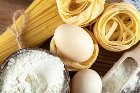 Two types raw pasta with eggs and bowl of flour on wooden board Stock Photos