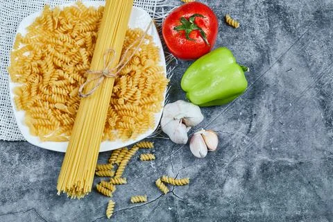 Two types of raw pasta on a white plate with tomato, pepper, and garlic Stock Photos