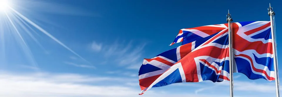 Two UK Flags Blowing in the Wind on Blue Sky with Clouds Stock Photos