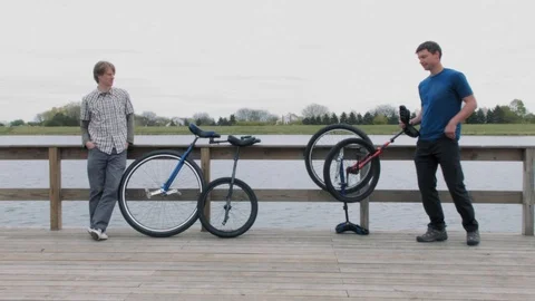 Two unicyclists taking a break by a lake Stock Footage 90054534