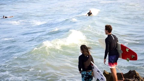 Two unidentified surfers watching waves and jumping into the water Видео 114145095