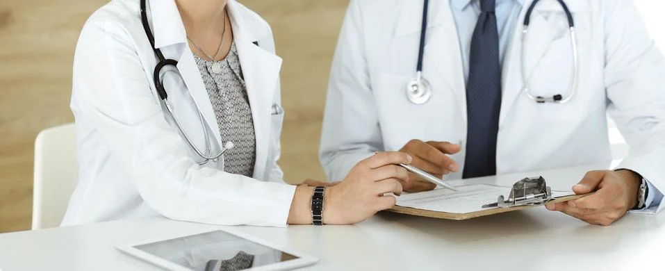 Two unknown doctors discussing treatment problems while sitting at the desk in Stock Photos
