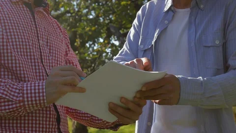 Two unrecognizable farmers conclude an agreement in the apple orchard Stock Footage 97701951