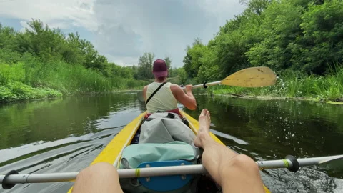 Two unrecognizable men are paddling along the river in a kayak, rowing with an Stock Footage 197433016