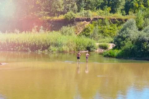 Two unrecognizable men are resting by the river, standing with their backs to 写真素材