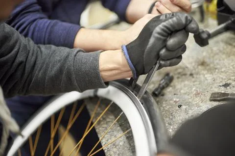 Two unrecognizable men remove an airless tire from a bicycle wheel. Stock Photos