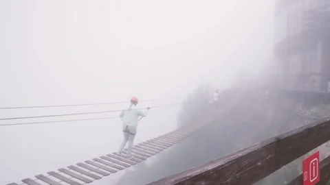 Two unrecognizable people walking on suspension hanging rope bridge in fog Stock Footage 282713160