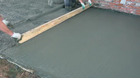 Two unrecognizable workers leveling the fresh concrete with a long wooden plank. Stock Footage 284843697