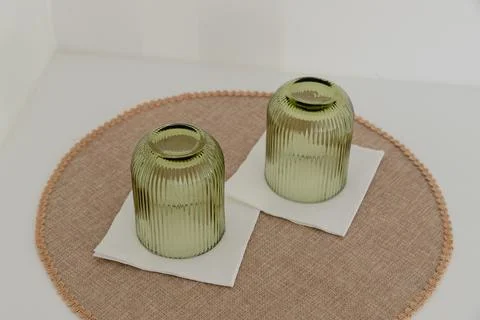 Two upside down green ribbed glass cups placed on white napkins over a round mat Stock Photos