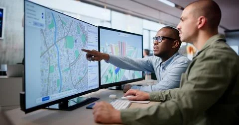 Two Urban Planners Use Computer Software To Analyze City Land Maps. 库存照片