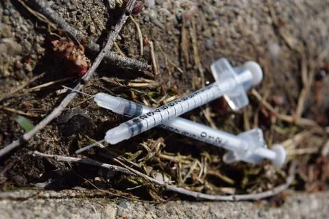 Two used discarded needles in a public park Stock Photos