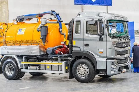 Two vehicles in an industrial setting, one orange truck with a containertan.. Photos