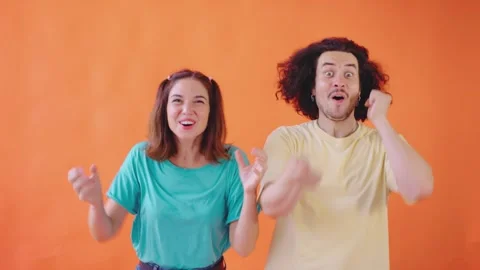 Two vibrant young adults express their enthusiasm against a lively orange Stock Footage 281123074