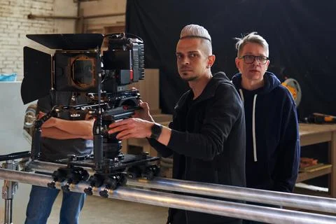 Two videographers stand behind a professional movie camera mounted on a camera Stock Photos