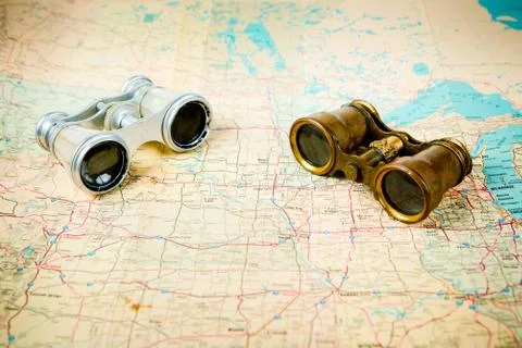 Two vintage binoculars on old map, one with brass metal body and second silve Stock Photos
