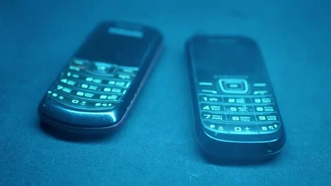 Two Vintage Button Mobile Phones Glowing In Mysterious Blue Smoke 库存影片 330110421