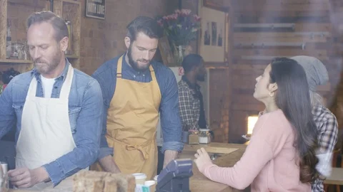 Two waiters serving coffee to customers and smiling at camera in coffee shop Video stock 108025044