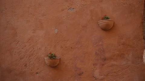 Two wall mounted ceramic flower pots with red violas on old orange wall, Italy 库存影片 123554403