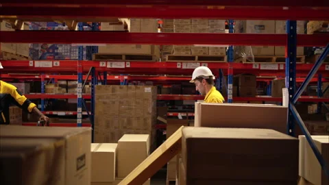 Two warehouse workers are lifting boxes of merchandise on a pallet jack to store Stock Footage 308937828