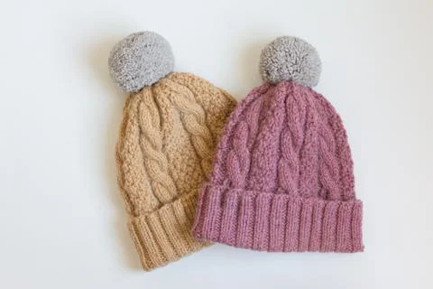 Two warm wool cap with pompon handmade beige and pink on a white table Stock Photos