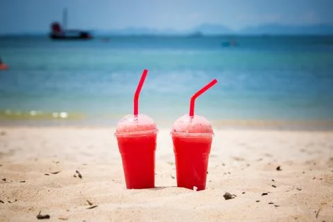 Two watermelon smoothies in disposable plastic cups with tubes. On a sandy tr Stock Photos