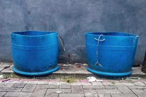 Two weathered blue plastic drums are positioned side by side on a textured .. Stock Photos