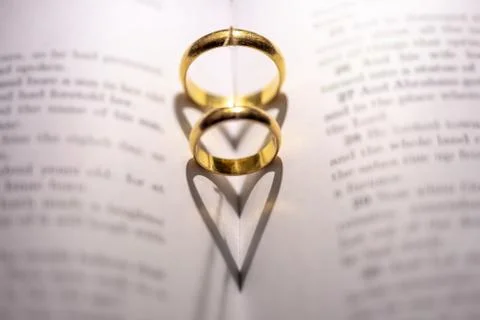 Two wedding Ring on the bible with shadow of heart shape on the page Stock Photos