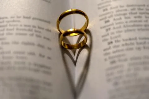 Two wedding Ring on the bible with shadow of heart shape on the page Stock Photos