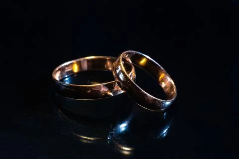 Two wedding rings of different sizes made in gold on the black mirror surface Stock Photos