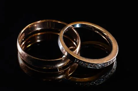 Two wedding rings of different sizes made in gold on the black mirror surface Stock Photos