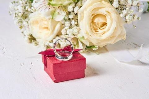 Two wedding rings of different sizes, a red gift box and a bride's bouquet li Stock Photos