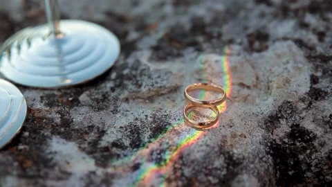 Two wedding rings lie on a rock near two silver glasses and shimmer in the Stock Footage 170607265
