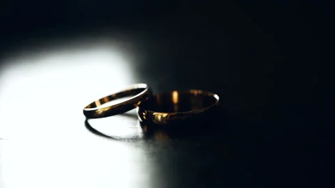 Two wedding rings lie on the table and illuminated by a bright beam of light Видео 105432813