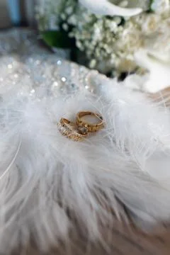 Two wedding rings placed on white feathers with flowers in the background d.. Stock Photos
