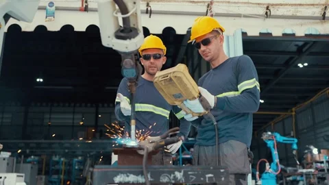 Two welders in hard hats work with a robotic arm together in a factory Stock Footage 340989204