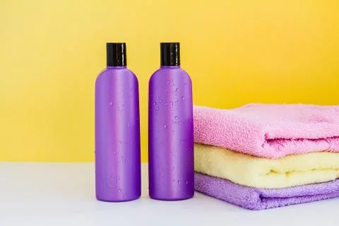 Two wet purple cosmetic bottles and three towels on a lilac background Foto stock