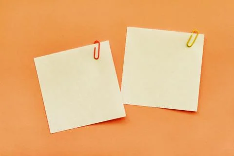 Two white adhesive note papers with clips on orange background Stock Photos