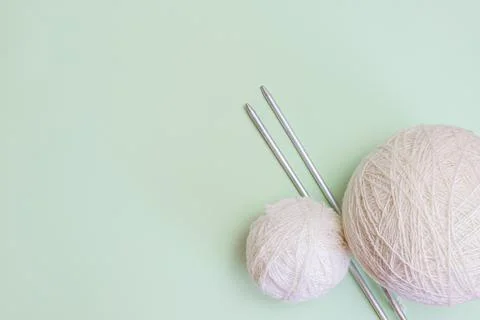 Two white balls of woolen thread and long metal needles on a light green back Stock Photos