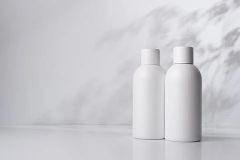 Two white bottles on a light background with shadows of plant leaves, represe Stock Photos