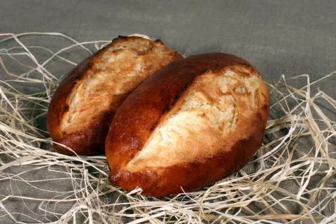 Two white bread lying in straw on grey linen tablecloth Stock Photos