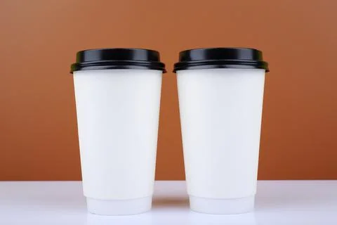 Two white cardboard cup of coffees on white table against brown background Stock Photos
