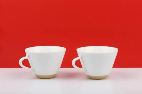 Two white ceramic coffee cups on white table against red background with space Stock Photos